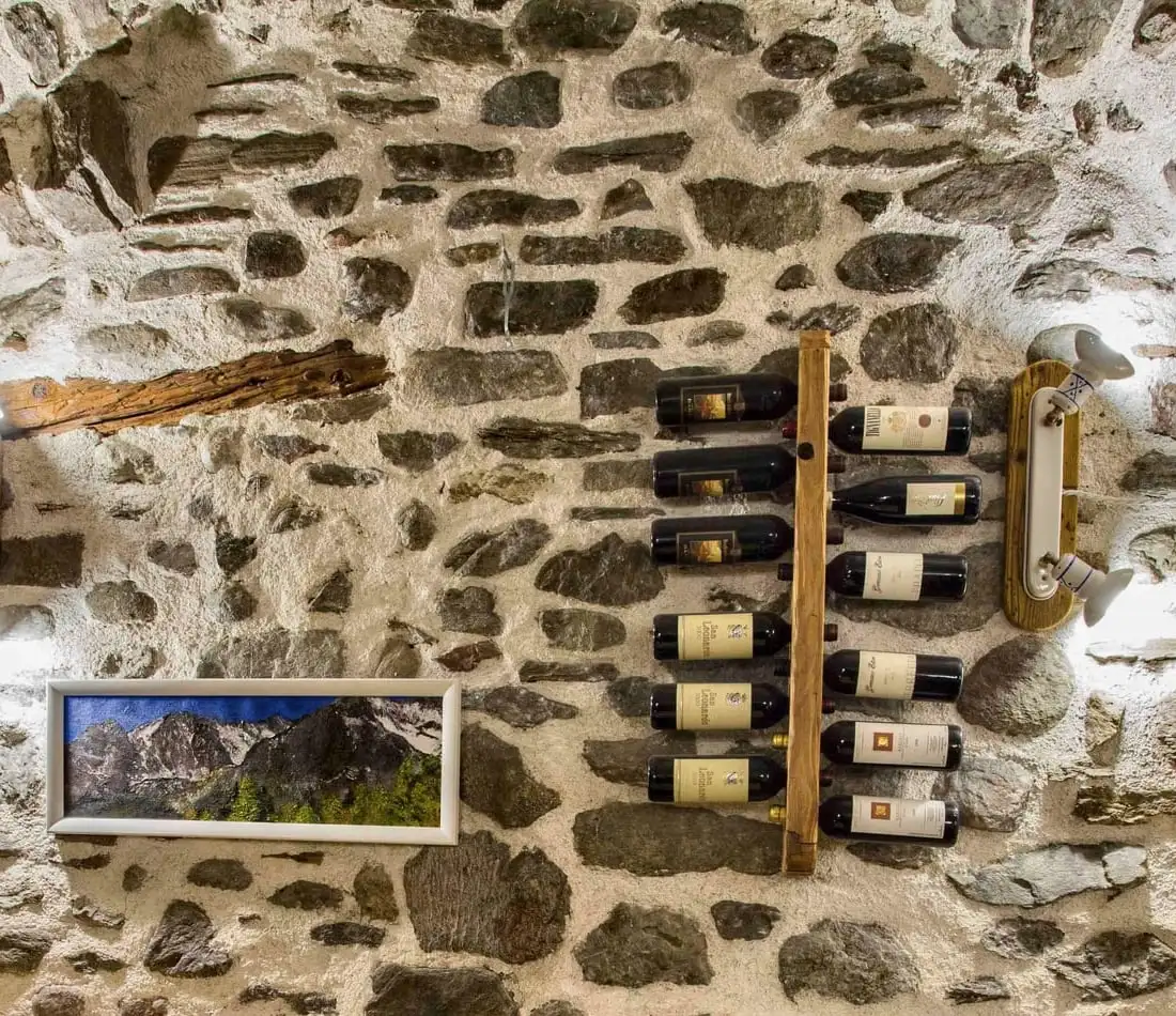 La volta in pietra della sala, con le bottiglie alla parete e un quadro di montagne